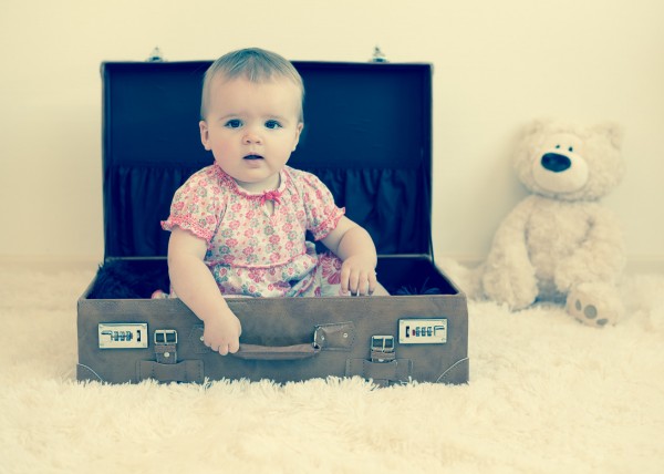 Enfant fille assise dans une valise avec un ourson peluche